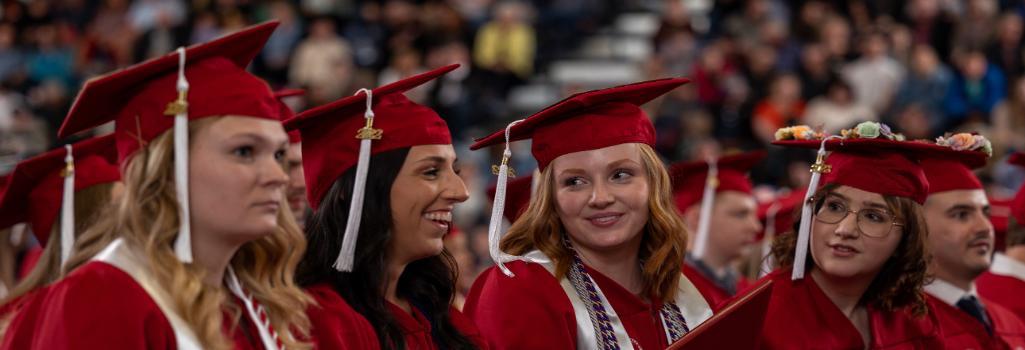 Four SVSU graduates talking and laughing at their graduation. 